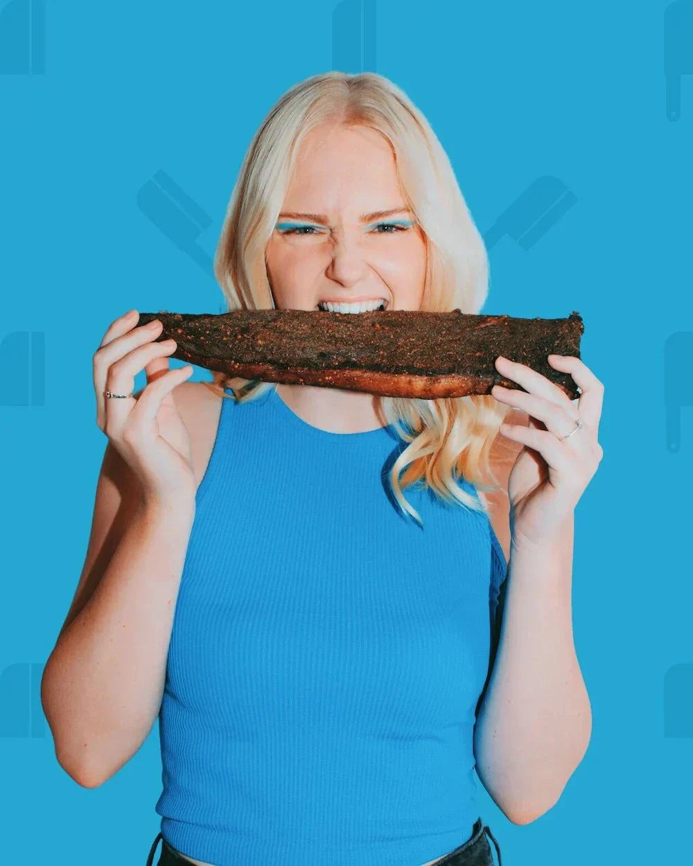 Photo of a blond girl taking a bite of a whole piece of biltong which will be sliced into sliced fatty biltong