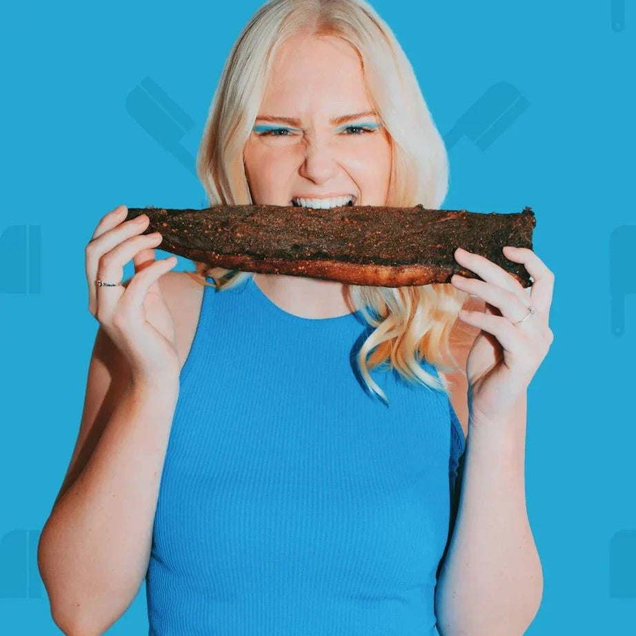 Photo of a blond girl taking a bite of a whole piece of biltong which will be sliced into sliced fatty biltong